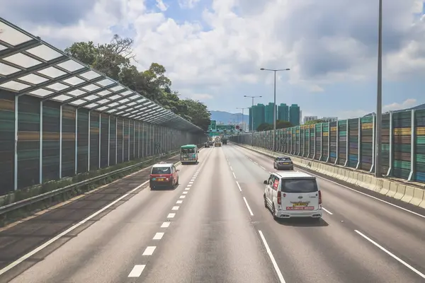 Çevresi yeşilliklerle çevrili, bakımlı bir otoyol boyunca giden araçlar.