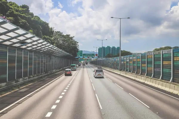 Çevresi yeşilliklerle çevrili, bakımlı bir otoyol boyunca giden araçlar.