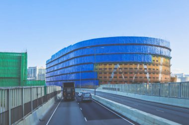 Mavi muşambaya sarılı bir inşaat alanını gösteren bir şehir manzarası.