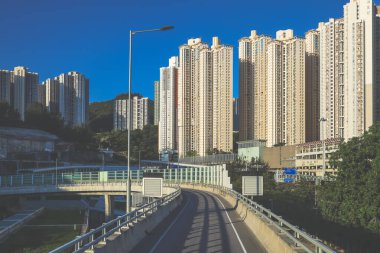 Güneşli şehir manzarasında yükseltilmiş bir yol yükselişte bir apartmana çıkıyor.