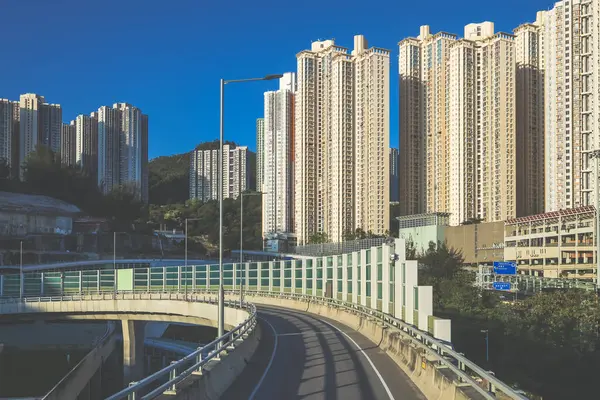 Güneşli şehir manzarasında yükseltilmiş bir yol yükselişte bir apartmana çıkıyor.