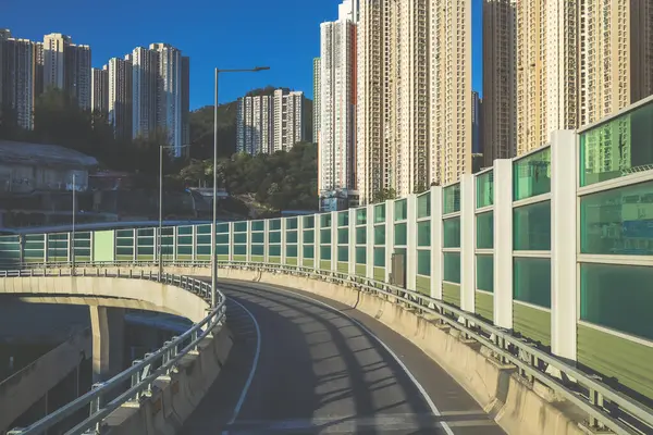 Güneşli şehir manzarasında yükseltilmiş bir yol yükselişte bir apartmana çıkıyor.