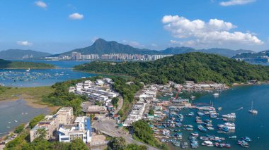 Yeşil tepelere yanaşmış teknelerle sakin bir sahil limanının canlı panoramik manzarası.