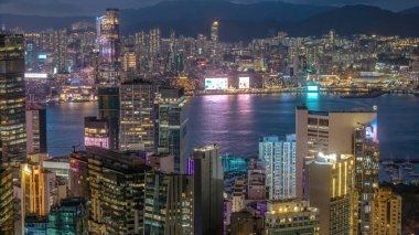 Aydınlatılmış Hong Kong gökdelenleri gece sergilenirken gökyüzü