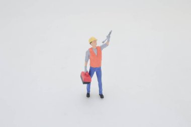 Güvenlik kaskı ve alet yeleği giymiş minyatür bir işçi figürü duruyor.