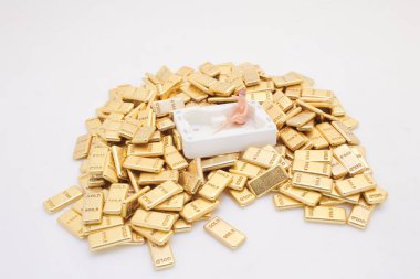 Küçük heykelcik, altın külçelerinin arasında beyaz bir küvette yatıyor.,