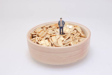 Servet ve başarı: Altın külçeleriyle dolu bir kasenin üzerinde kendinden emin duran minyatür bir insan figürü.,