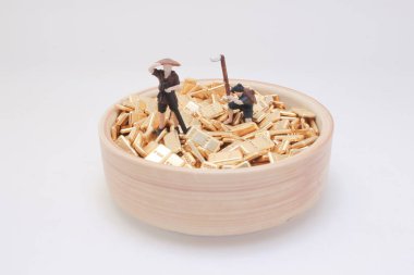 Tahta bir kase içinde altın külçelerin üzerinde duran minyatür figürlerin yakın plan görüntüsü.,