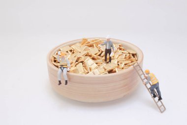 Altın külçeleriyle dolu bir kâseyi yöneten işçilerin minyatür heykelleri.,