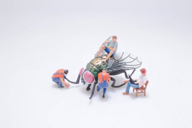 Büyük bir sinek modeliyle uğraşan minyatür insanların yaratıcı tasviri,