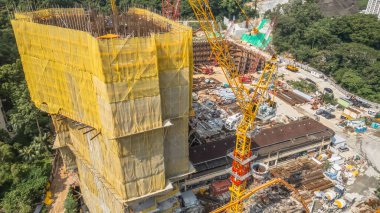 Sarı kaplamalı bir bina ve vinçlerin bulunduğu aktif bir inşaat alanı.