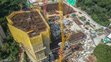 Sarı kaplamalı bir bina ve vinçlerin bulunduğu aktif bir inşaat alanı.