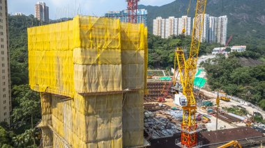 Sarı kaplamalı bir bina ve vinçlerin bulunduğu aktif bir inşaat alanı.