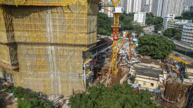 Sarı kaplamalı bir bina ve vinçlerin bulunduğu aktif bir inşaat alanı.