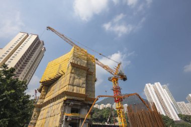 Sarı kaplamalı bir bina ve vinçlerin bulunduğu aktif bir inşaat alanı.