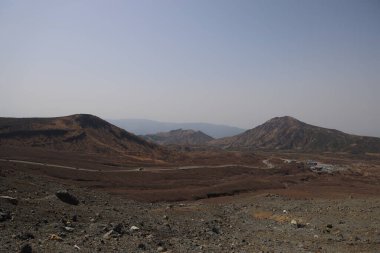 Dağılmış kayalar ve alçak bitki örtüsüyle geniş çorak bir arazi.