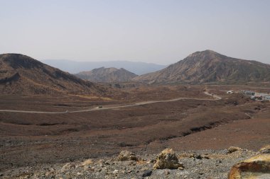 Dağılmış kayalar ve alçak bitki örtüsüyle geniş çorak bir arazi.