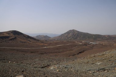 Dağılmış kayalar ve alçak bitki örtüsüyle geniş çorak bir arazi.