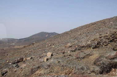 Dağılmış kayalar ve alçak bitki örtüsüyle geniş çorak bir arazi.