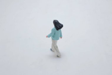 Deri gömlekli, beyaz pantolonlu, yürüyen bir kadın figürü.