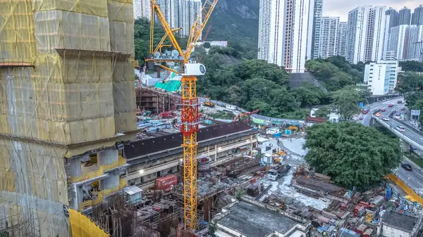 Sarı kaplamalı bir bina ve vinçlerin bulunduğu aktif bir inşaat alanı.