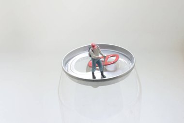 Küçük bir işçi heykeli bir soda kutusunun kapağında duruyor.,