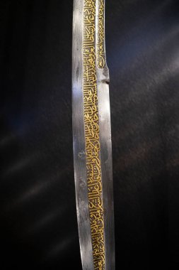 Siyah arka planda izole edilmiş Arapça kaligrafi olan bir kılıç yüzeyine yakın plan..