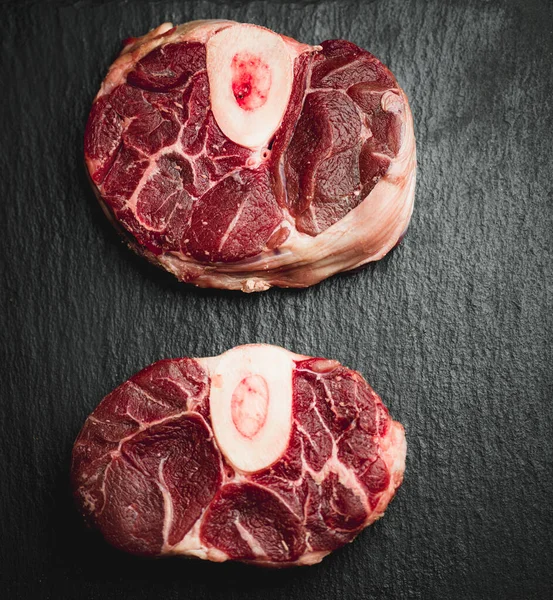 raw beef osso buco rib eye steaks on a dark background, top view, close up, horizontal osso buco , milanese food italian food typical , copy space