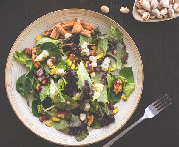 salad with chicken, arugula, avocado, green peas and walnuts on a black background, top view,