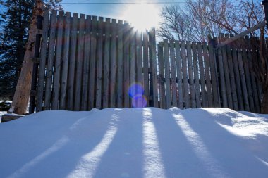 Güneş çitin arkasından yükseliyor. Önünde kar yağışı var. Yeni yağmış kardan.