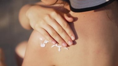 Genç bir kadın omzuna güneş kremi sürüyor.