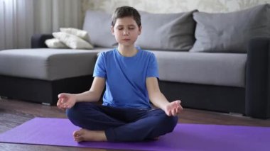 Çocuk evde yoga minderine oturmuş meditasyon yapıyor.