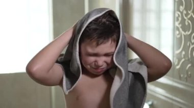 Çocuk banyoda havluyla saçını siliyor..