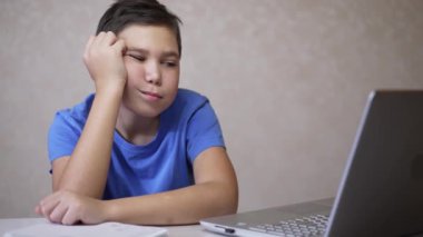 Yorgun öğrenci çevrimiçi dersler alıyor, kafası karışık ve bilgisayar ekranına bakıyor.