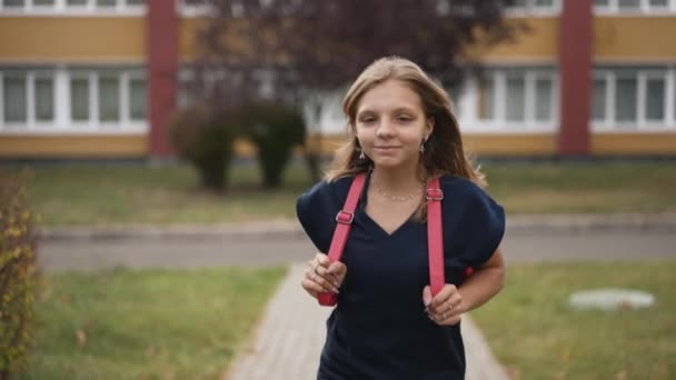 一个带着粉色背包的女孩从学校跑了出来 — 图库视频影像