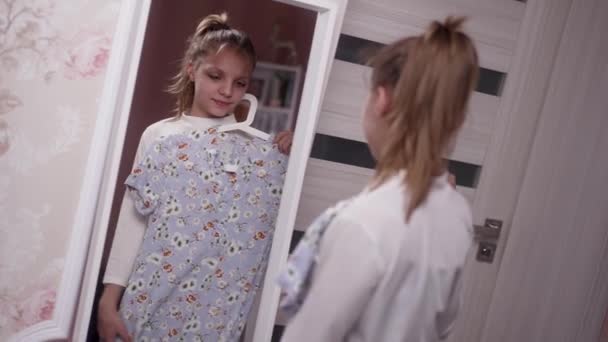 一个年轻姑娘站在一间明亮的室内房间里 在一面全长的镜子里审视自己的倒影时 她把一件花衣服举到自己身上 — 图库视频影像