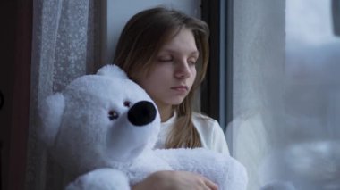 Genç bir kız pencerenin yanında dikilirken görülüyor, dışarıya bakıyor. Düşüncelere dalmış camın ötesindeki manzarayı izlerken dalgın görünüyor..