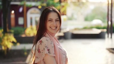 Uzun saçlı ve güneş gözlüklü bir kadın şehir caddesinde yürüyor.