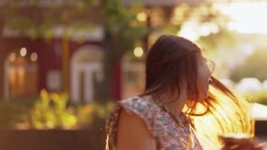 Uzun saçlı ve güneş gözlüklü bir kadın şehir caddesinde yürüyor.