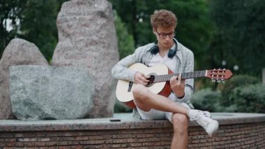 Parkta gitar çalan kıvırcık saçlı genç bir adam.