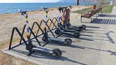 Güneşli bir günde plaja yakın park etmiş elektrikli scooterlar.