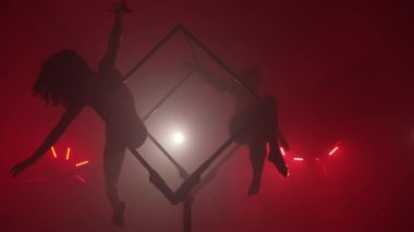 Sahne ışıkları altında büyük bir kübün içinde senkronize akrobatik numaralar sergileyen iki yetenekli kadın..