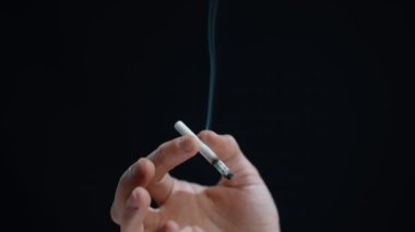 Sigara içen bir adamın elinde yanan bir sigara tutarken çekilmiş yakın plan bir fotoğraf..