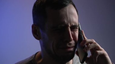 Loş bir odada yalnız bir adam, telefonda gözyaşlarıyla konuşuyor, yüzü umutsuzluk ve sessiz ızdırapla kavrulmuş..