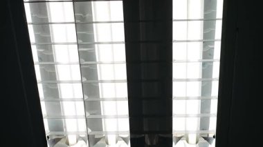 Tavanda bir neon tüpü titreşen, dengesiz bir ışık yayar.