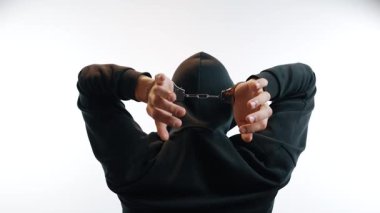 Kelepçeli adam, ellerini aşağıda tutuyor.