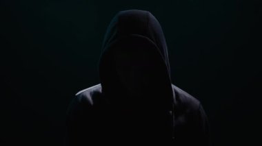 Kapüşonlu bir adam zifiri karanlık bir odada duruyor. Kimliği gölgeler tarafından siliniyor. Gizlilik ve sessiz tetikte..
