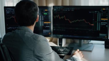 Gözlüklü bir adam gerçek zamanlı finansal tabloları inceliyor, modern ticaret ortamında uzmanlığı ve stratejik karar verme mekanizmasını yansıtıyor..