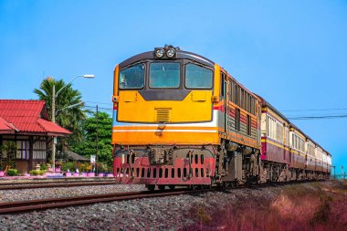 Tren istasyonunda dizel lokomotifle giden yolcu treni. Bina halka açıktır.)