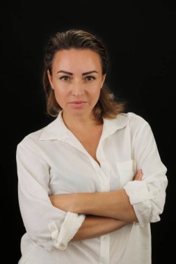 Beyaz bluzlu, koyu renk gözlü, kollarını çapraz yapmış güzel bir kadın kendinden emin bir şekilde ileriye bakıyor..